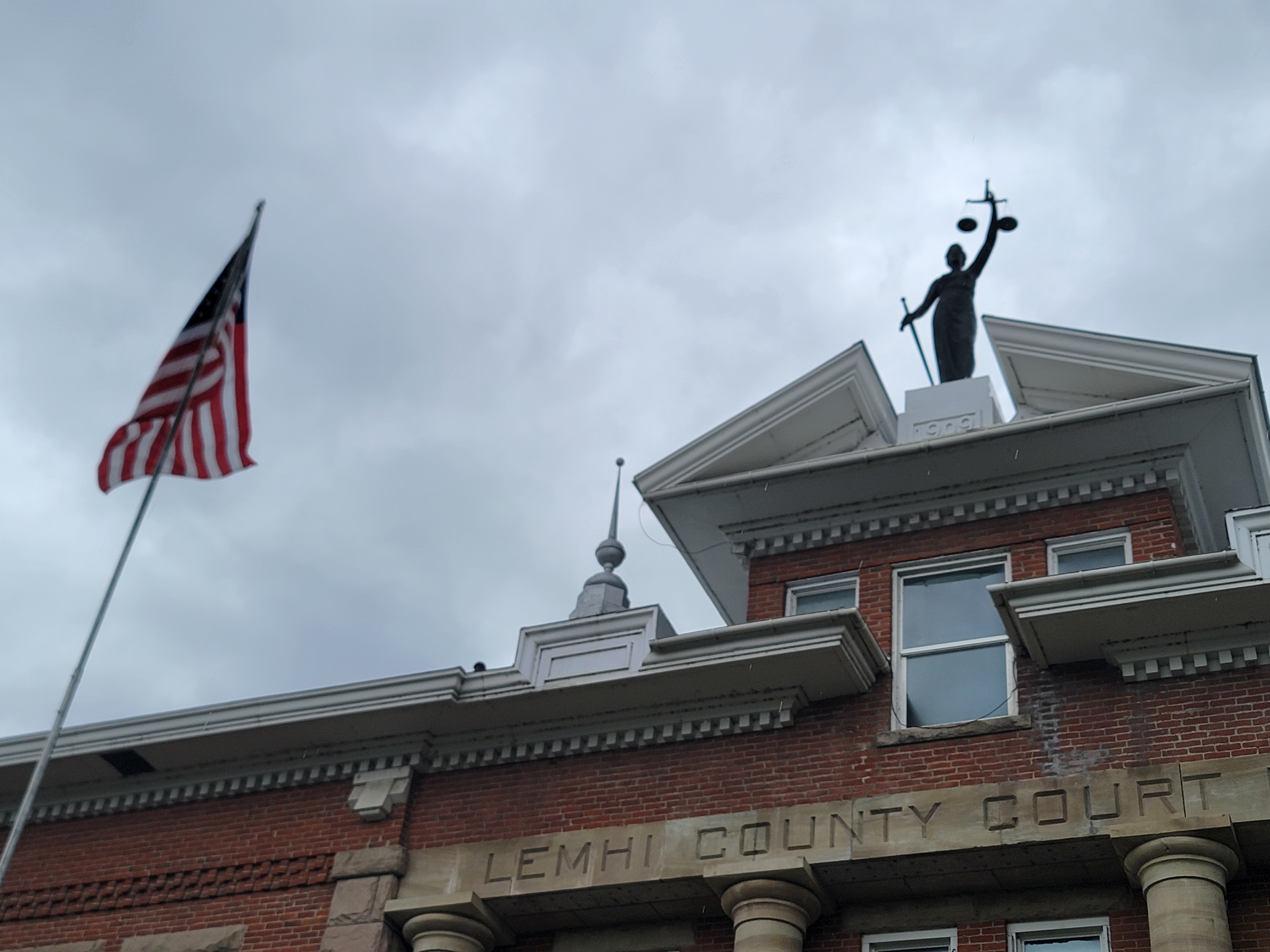 Lemhi County Courthouse in Salmon, Idaho, with the Lady Justice statue and American flag displayed above the historic courthouse entrance.